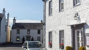 A white building with a clock tower, a parked car, and potted plants. - The Murray Arms Hotel (Castle Douglas)