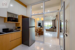 Uma cozinha moderna com frigorífico embutido, armários de madeira e uma zona de refeições com porta de vidro que dá para uma sala de estar.