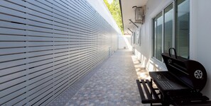 Ein überdachter Außenbereich mit Grill, einer Bank und einem Weg.