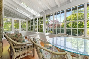 Ein Wintergarten mit Korbmöbeln, großen Fenstern und einem Glastisch.
