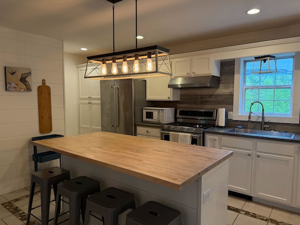 A modern kitchen with a central island, bar stools, stainless steel appliances, and a window with a view.