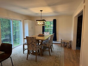 A dining room with a wooden table, floral chairs, a chandelier, and large windows with a view of trees.