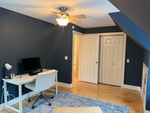 A room with a desk, computer, and a ceiling fan. There are two white doors and a window.
