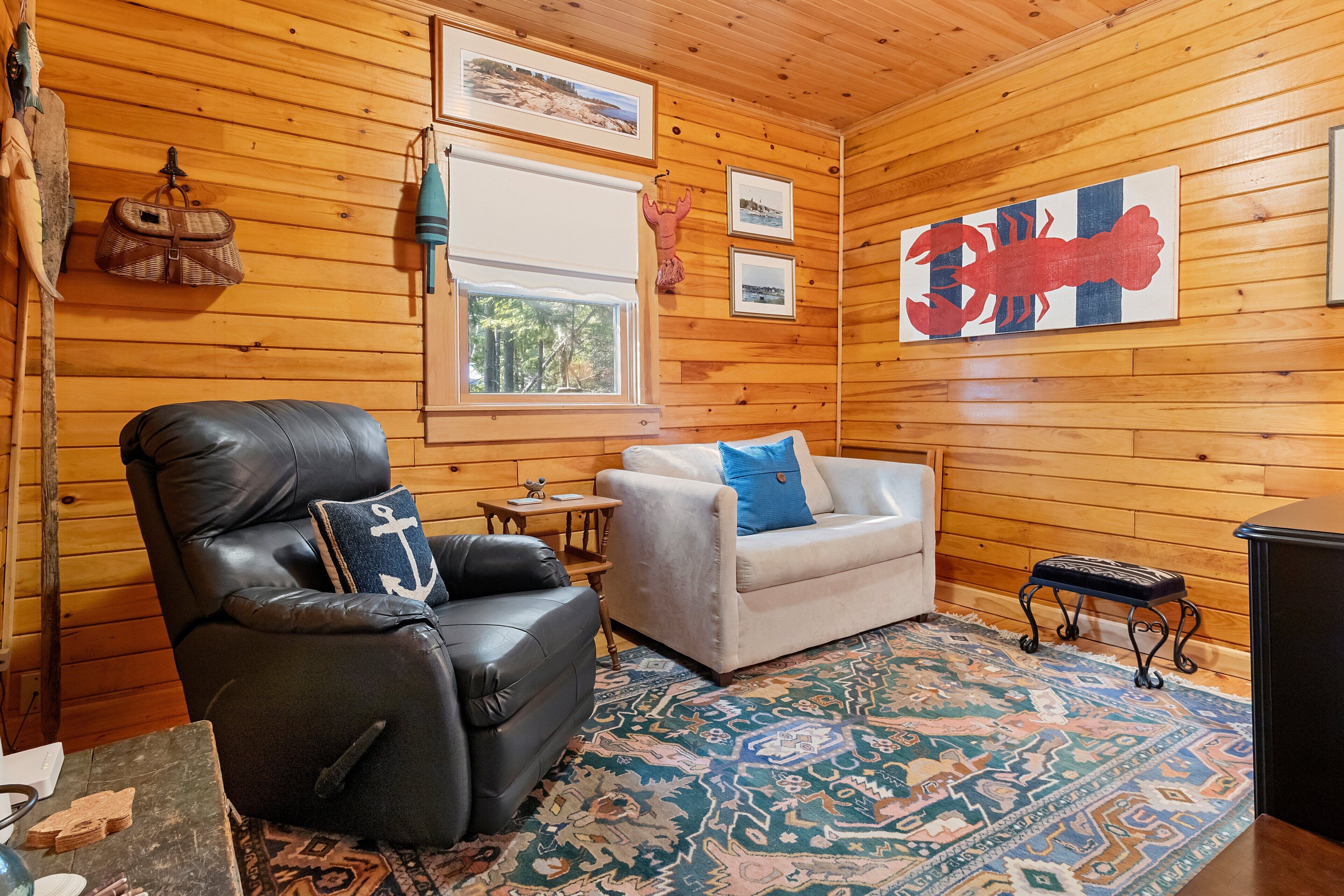 Ein gemütliches Zimmer mit Ledersessel, weißem Sofa, einem gemusterten Teppich und Holzwänden.