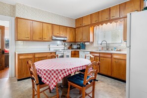Une cuisine avec des meubles en bois, un four blanc et une table recouverte d’une nappe à carreaux.