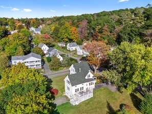 A residential area with houses surrounded by trees and a hill in the background. - One Atlantic- | 5BR harbor view Maine home, close to town, deck (Boothbay Harbor)