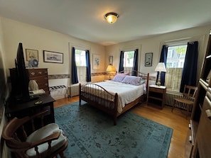 Ein Schlafzimmer mit einem hölzernen Bett, Nachttischen, einem Schreibtisch, einem Sessel und einer Heizung.