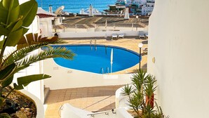 Zona de piscina con vista al mar y un pueblo al fondo.
