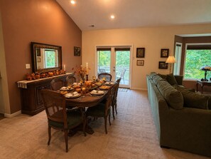 A dining area with a table set for four, a sofa, and a view of the outdoors through a sliding glass door. - Millie's Lake Lure Lodge - Private Dock, Spacious, Bathrooms for Every Bedroom! (Lake Lure)