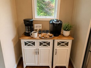 A kitchenette with a coffee maker, a mug, a plate of pastries, and a sign. - Millie's Lake Lure Lodge - Private Dock, Spacious, Bathrooms for Every Bedroom! (Lake Lure)
