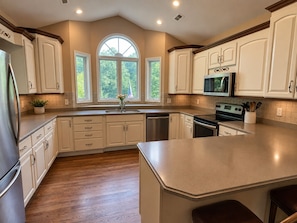 A kitchen with white cabinets, a large island, a microwave, and a dishwasher. - Millie's Lake Lure Lodge - Private Dock, Spacious, Bathrooms for Every Bedroom! (Lake Lure)