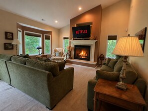 A living room with a fireplace, a television displaying 'NETFLIX,' and a sofa. - Millie's Lake Lure Lodge - Private Dock, Spacious, Bathrooms for Every Bedroom! (Lake Lure)