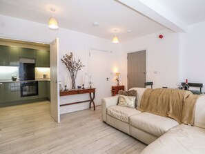 Ein modernes Wohnzimmer mit einer Couch, einem Esstisch mit Stühlen, einer Küchenzeile und Pendelleuchten.