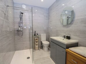 Ein modernes Badezimmer mit einer gläsernen Duschkabine, Toilette, Waschbecken mit Spiegel und einem Holzkabinet.