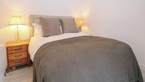 Ein ordentlich bezogenes Bett mit Kopfteil, zwei Nachttischlampen, einem Holznachttisch mit Schubladen und einer strukturierten Decke.