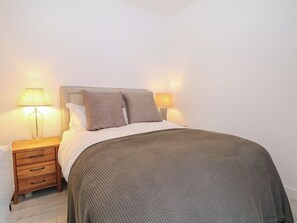 Ein ordentlich bezogenes Bett mit Kopfteil, zwei Nachttischlampen, einem Holznachttisch mit Schubladen und einer strukturierten Decke.