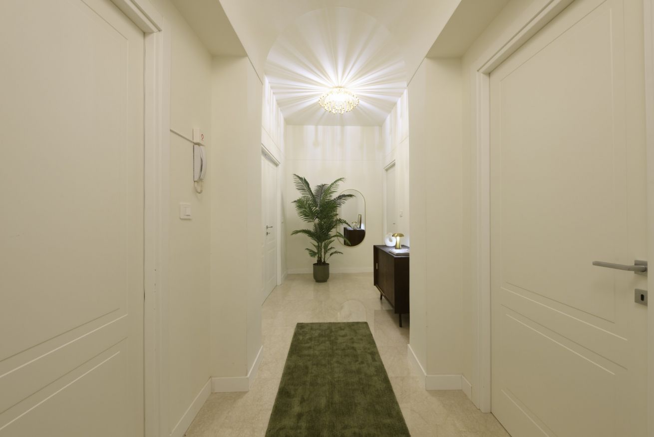 Un couloir avec un tapis vert, une plante en pot, un meuble et un luminaire au plafond.