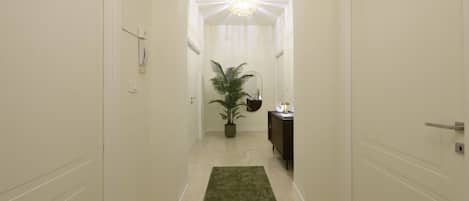 A hallway with a green carpet, a potted plant, a cabinet, and a ceiling light fixture.