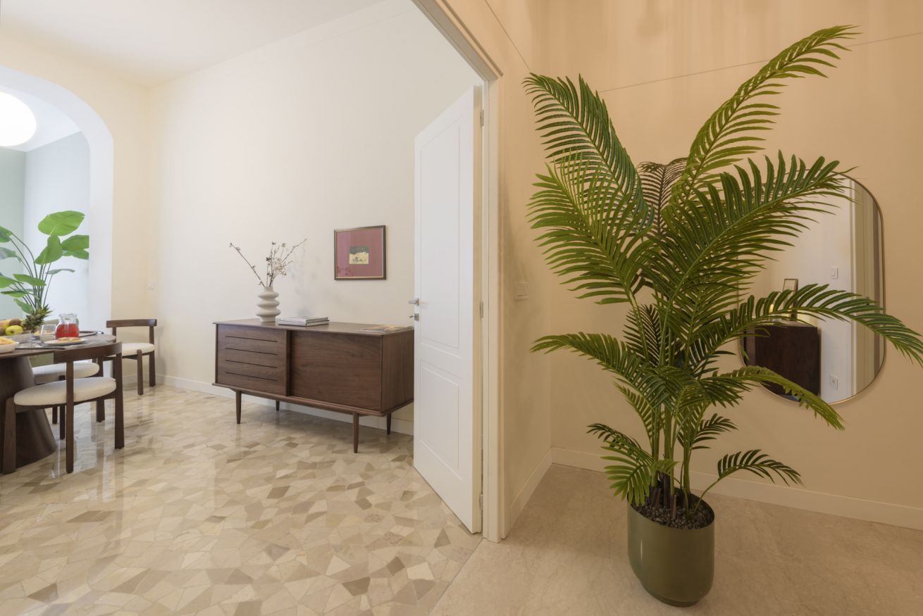 A room with a dining table, chairs, a cabinet, a potted plant, and a mirror on the wall.