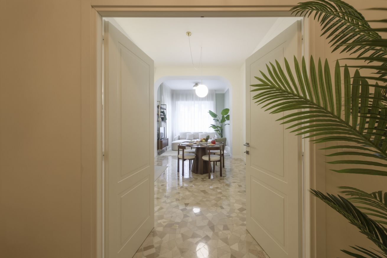 Un pasillo que conduce a un comedor con una mesa, sillas, una lámpara en el techo y una planta.
