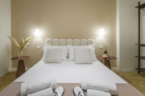 Ein ordentlich bezogenes Bett mit weißen Leinen, zwei Nachttische mit Lampen, eine Champagnerflasche und eine Vase mit Trockenblumen.
