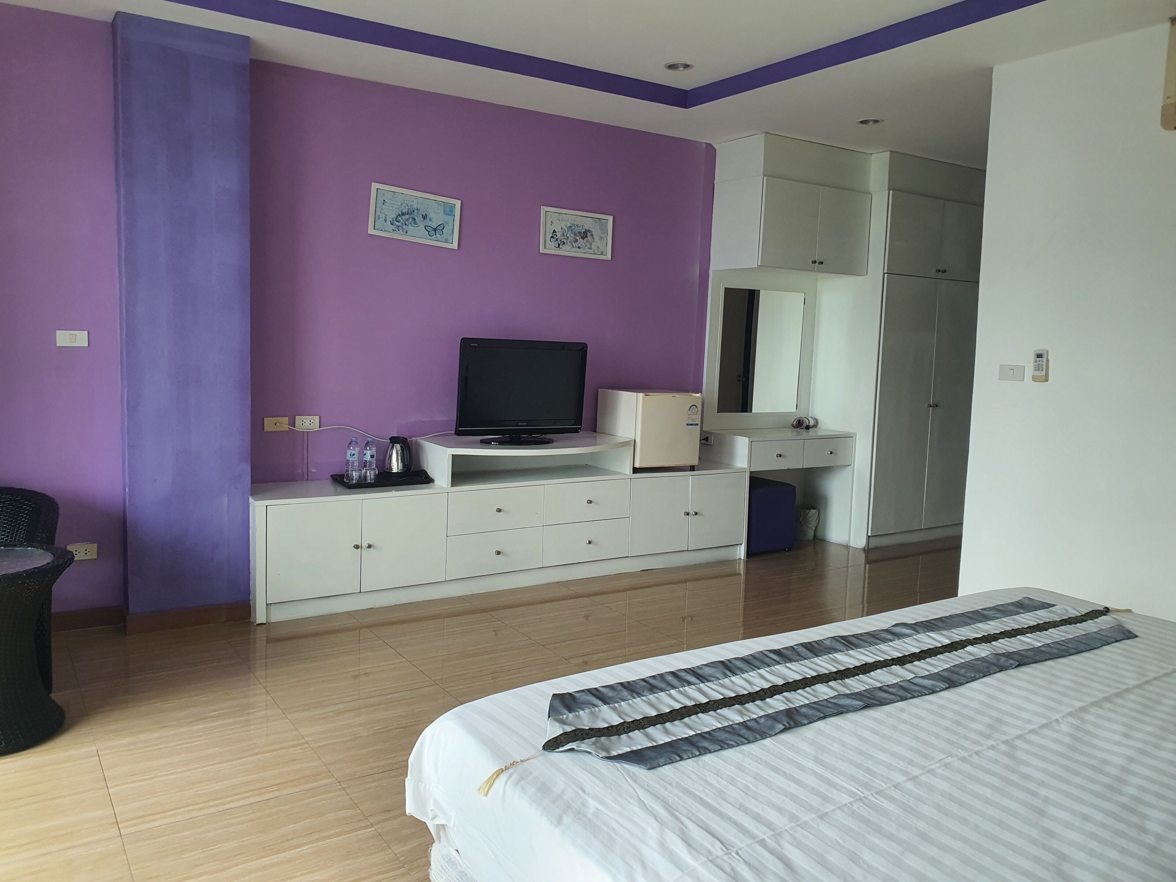 A bedroom with a bed, a TV, a dresser, a mirror, and a wardrobe.
