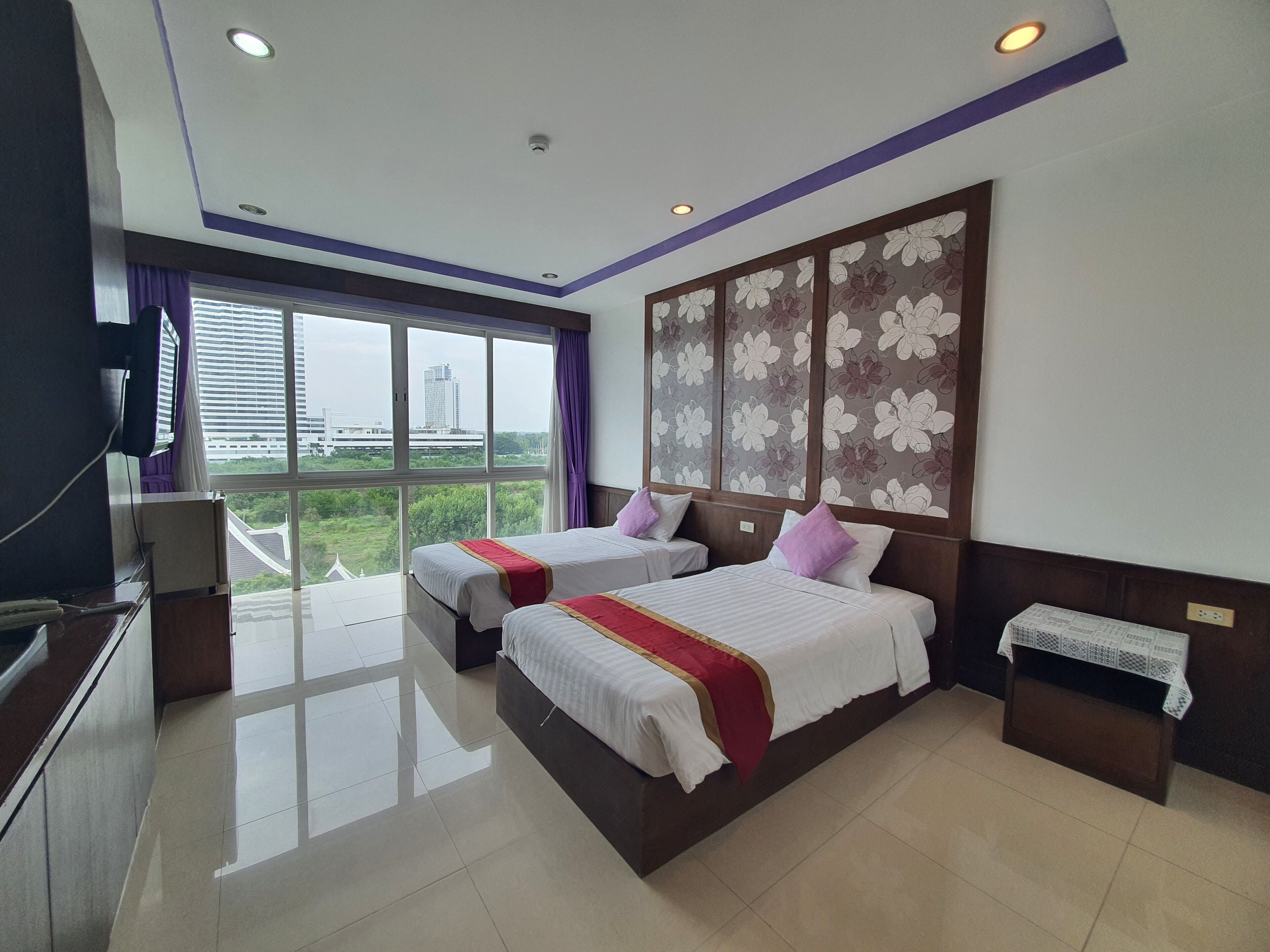 A hotel room with two beds, a large window with a view, a flat-screen TV, and a small table.