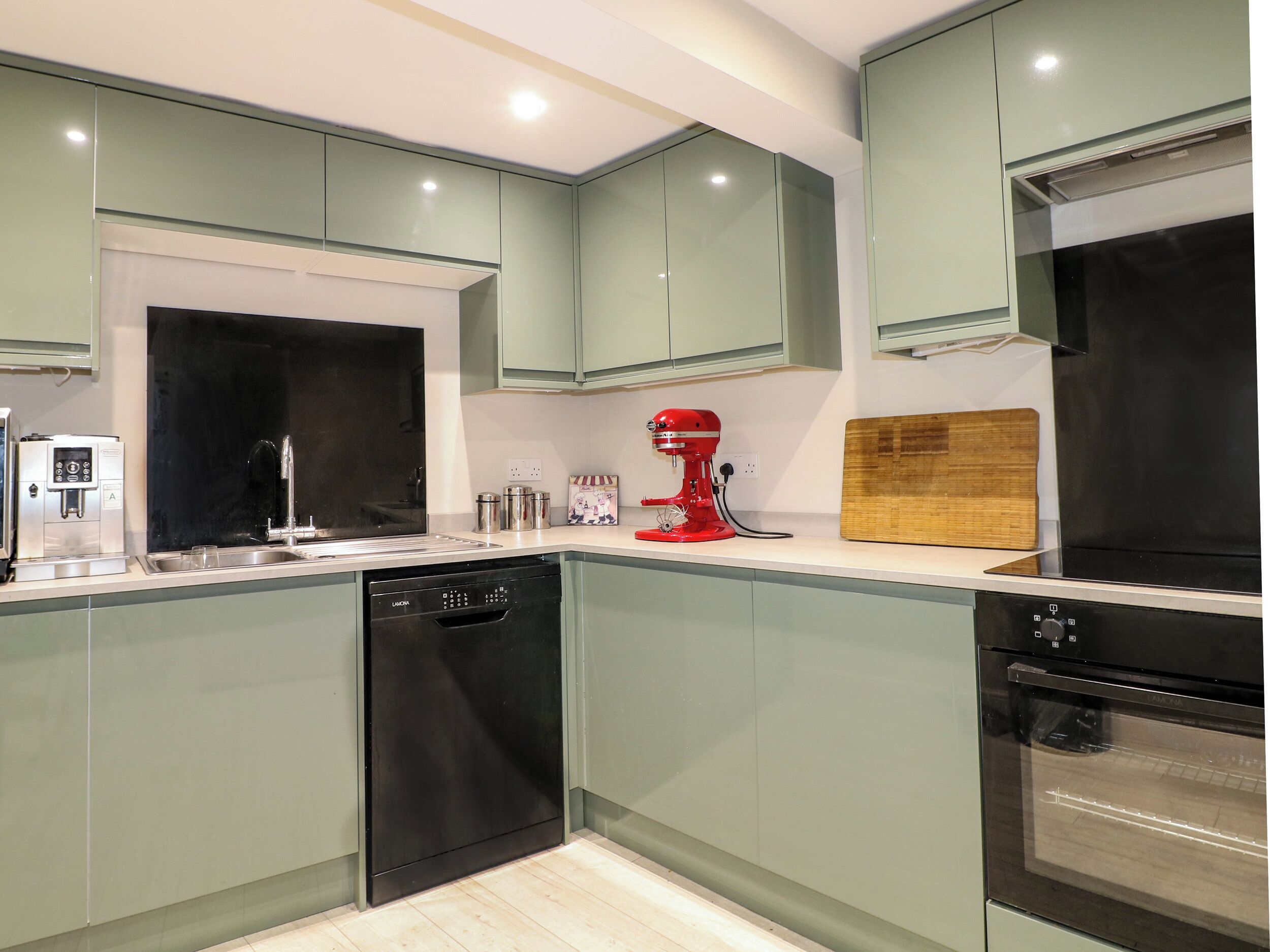 Een moderne keuken met een vaatwasser, een rode standmixer en een houten snijplank.
