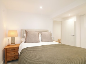 A bedroom with a bed, a bedside table with a lamp, a nightstand, and a door. - The Old Granary (Southampton)
