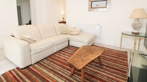 Een woonkamer met een hoekbank, een houten salontafel, een gestreept tapijt, een lamp en een lijst met een foto aan de muur.