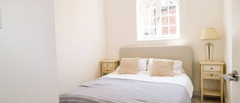 A bedroom with a single bed, a nightstand, a lamp, and a window with a view of a brick building.