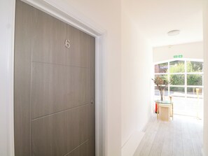 A hallway with a closed door marked with the number 6, leading to a bright room with a window and a glass table with a vase. - The Old Granary (Southampton)
