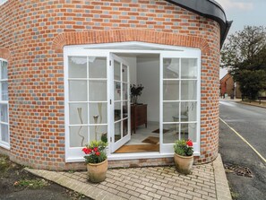A brick building with a white door and windows, a small wooden bench, and two potted plants. - 2 Bed (Southampton)