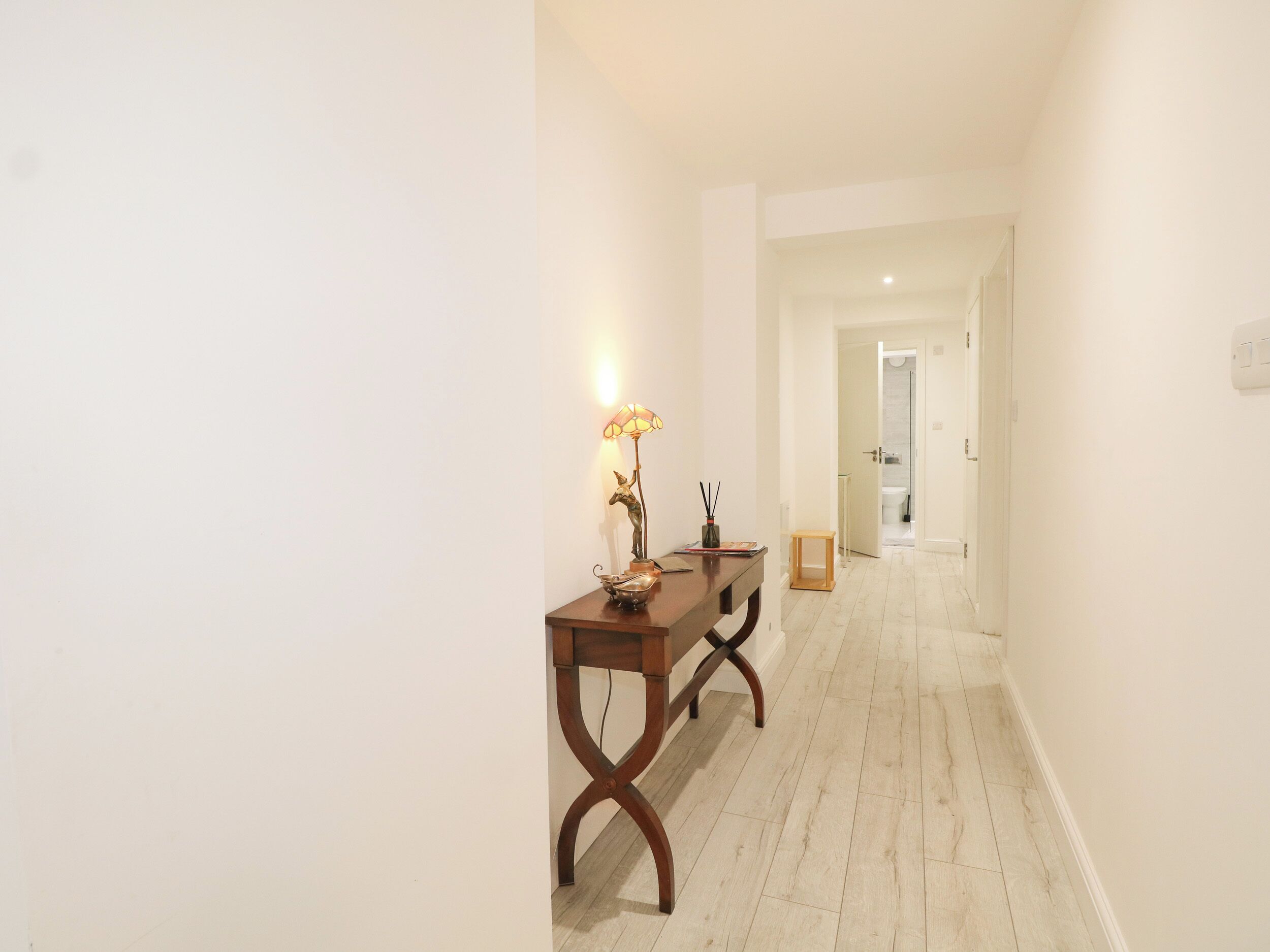A hallway with a wooden table and a lamp, leading to a bathroom.