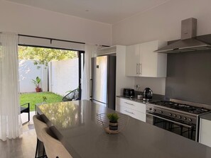 A modern kitchen with a central island, stainless steel appliances, and a view to a backyard. - Serenity Falls Estate luxury 2 Bedroom Getaway (Victoria Falls)