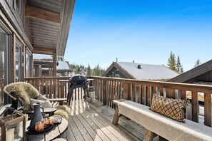 Eine Holzterrasse mit Grill, einer Bank und einem Fellstuhl.