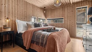 A wooden-paneled bedroom with a bed, bedside table, and a window.