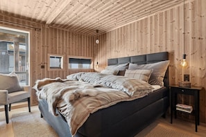 Ein Schlafzimmer mit Holzwänden, einem Bett, einem Sessel, einem Nachttisch und einem Fenster.