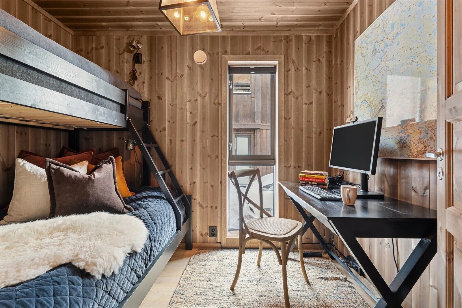 A wooden cabin interior with a bunk bed, desk, chair, and a map on the wall.
