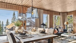A modern interior with a wooden ceiling, large windows, a dining area, and a seating area with a view of trees.