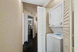 Een wasruimte met een wasmachine en droger, een deur naar een keuken, en een vloer met een patroon.