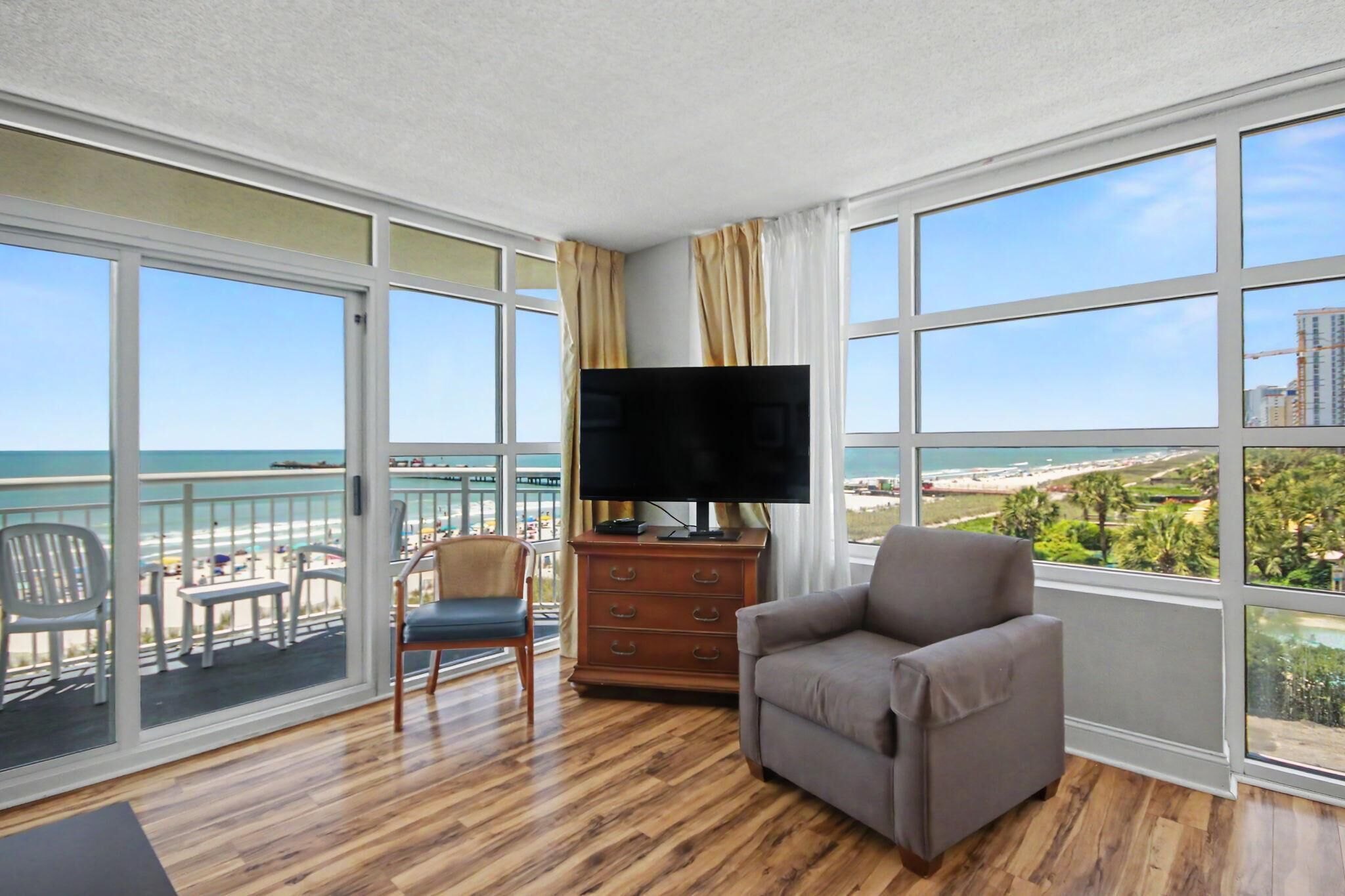 A room with a balcony, a TV, a sofa, and a wooden floor.
