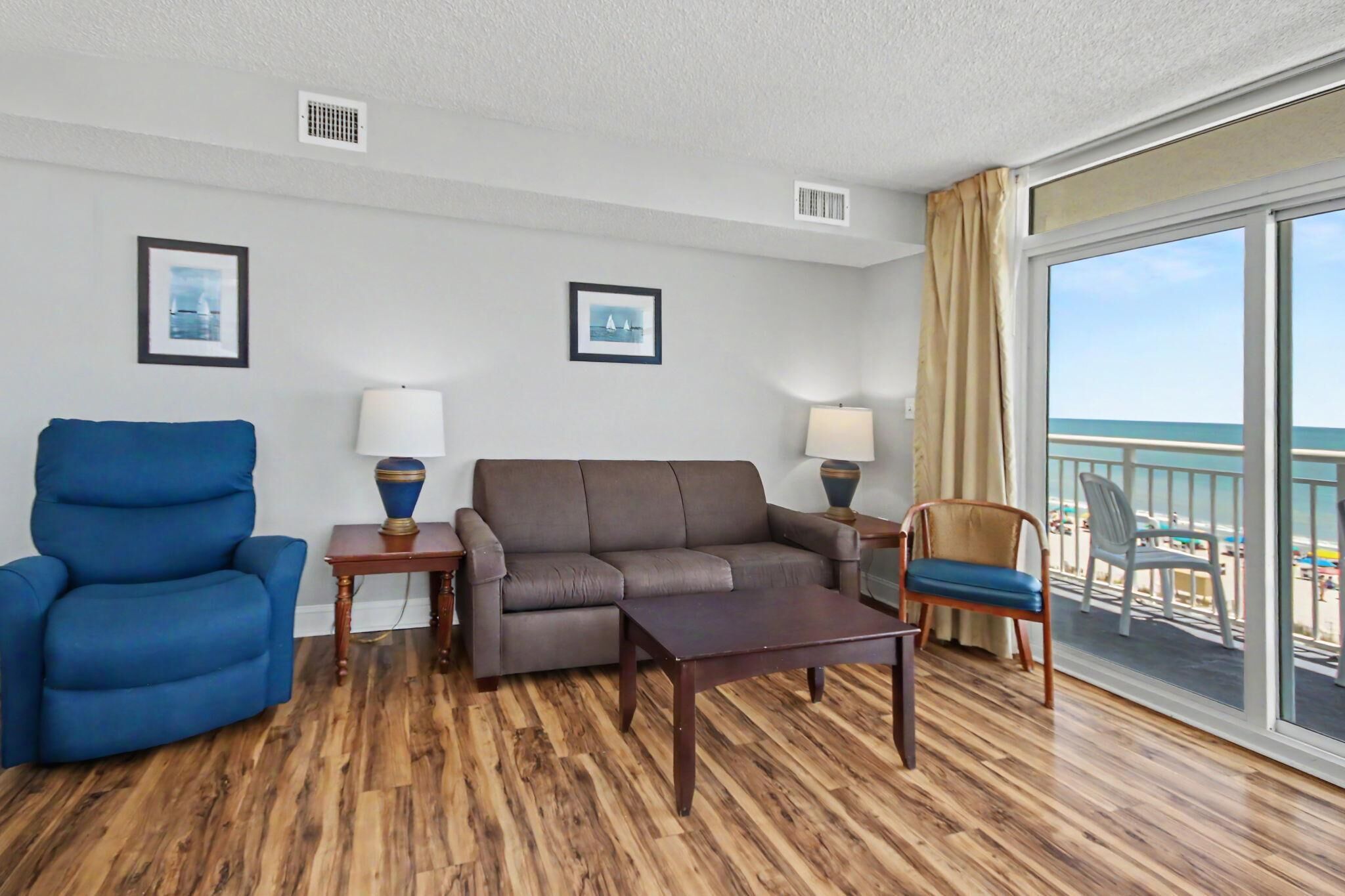 Ein Zimmer mit einer Couch, einem Sessel und Blick auf den Strand durch große Fenster.