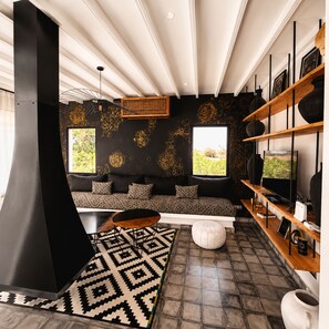 A modern living room with a black sofa, a large black fireplace, and a wooden shelf with decorative items. - Palais Oriella (Essaouira)