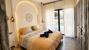 A bedroom with a bed, a decorative wall, a pool view, and a wardrobe. - Palais Oriella (Essaouira)