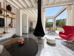 Ein modernes Interieur mit Kamin, einem Essbereich mit Blick ins Freie und einem roten Sessel.
