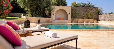 A poolside area with lounge chairs, a small seating area with cushions, and a decorative wall.