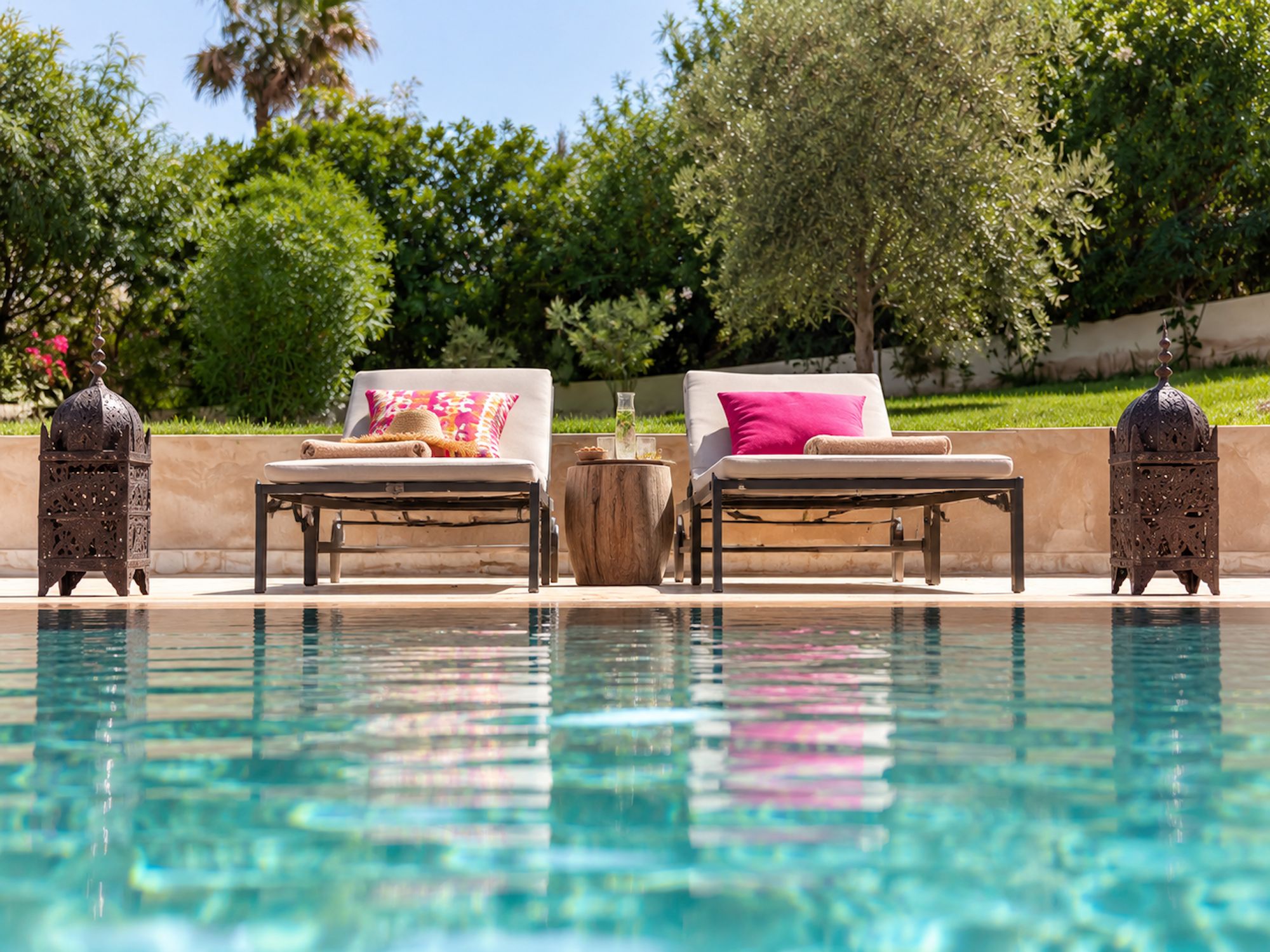 Un espace aménagé au bord de la piscine, comprenant deux chaises longues, une table en bois et des lanternes décoratives.