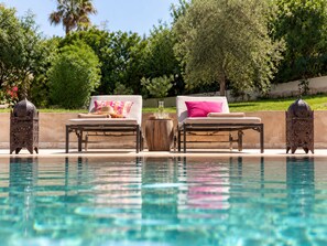 Ein Poolbereich mit zwei Liegestühlen, einem Holztisch und dekorativen Laternen.
