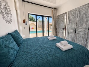 Ein Schlafzimmer mit einem großen Bett, Blick auf einen Swimmingpool und einer Tür, die nach draußen führt.